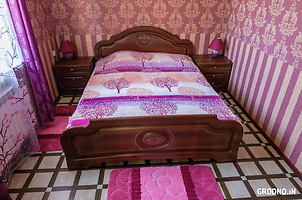 Сиреневая спальня. Большая двуспальная кровать, 2 прикроватные тумбочки, справа столик с зеркалом, стулья.